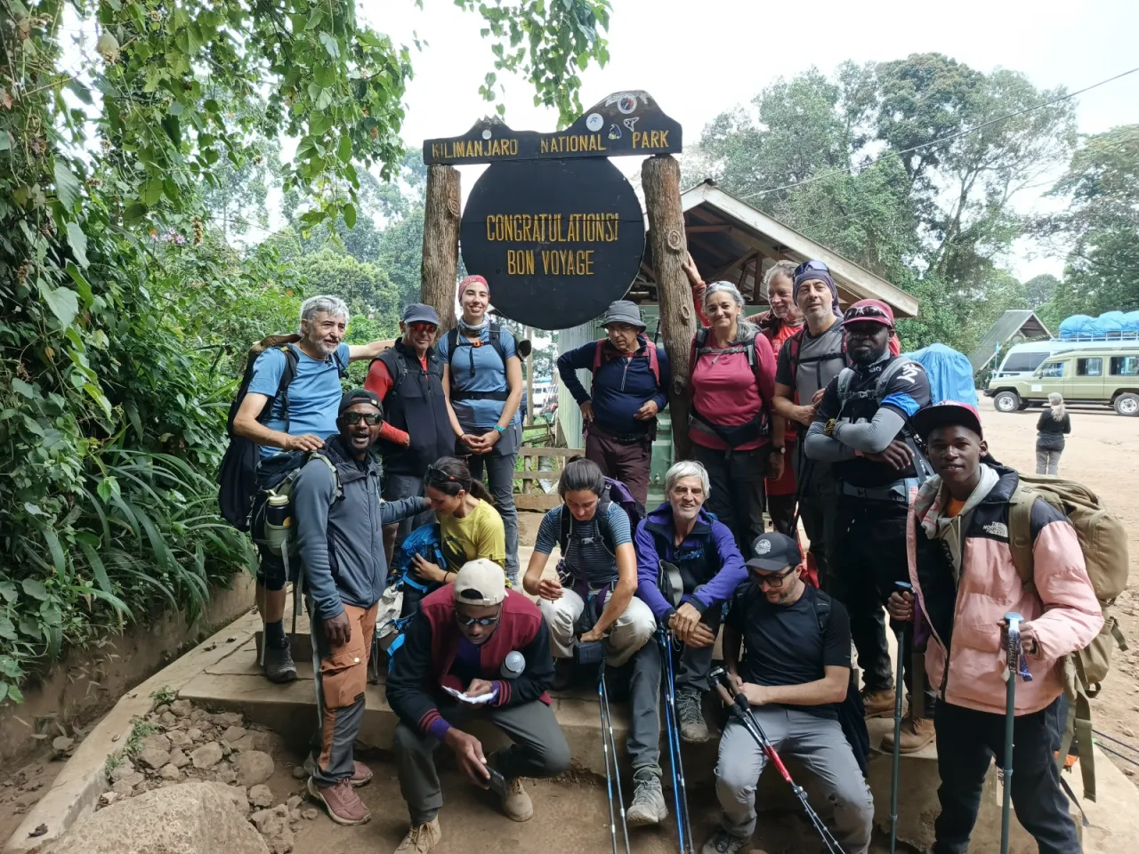 Smiling climbers and guides beside a Kilimanjaro National Park sign reading Congratulations! Bon Voyage