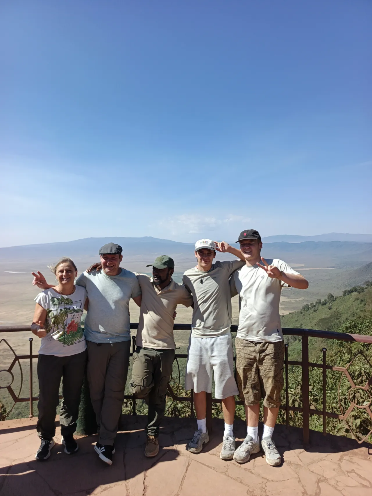 Five travellers with their guide at a railed viewpoint above a vast crater floor
